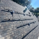 Roof with horizontal solar mounting rails and wiring on dark shingle tiles under a sunny sky.