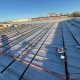Rooftop under construction with parallel cables and mounting rails for solar panels on a metal roof under a clear blue sky