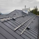 Metal standing-seam roof with solar mounting rails and wiring installed; chimney wrapped in Tyvek is visible in the background.